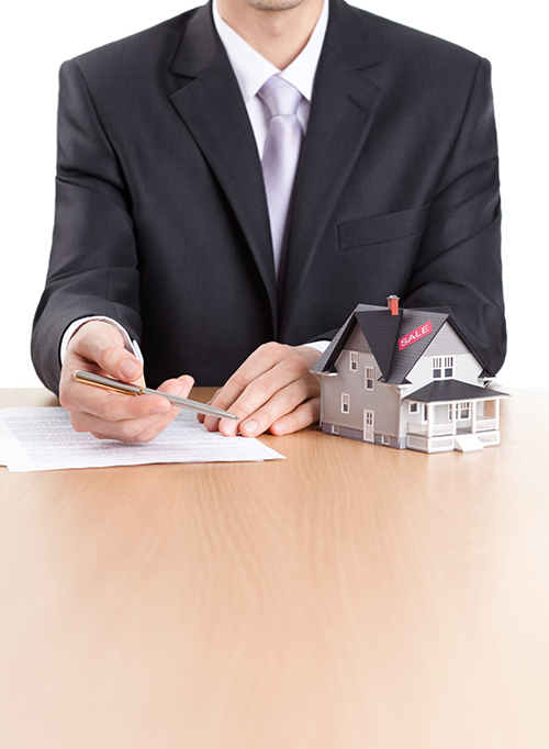 Business man signs a contract next to a model of a home Business man signs a contract next to a model of a home