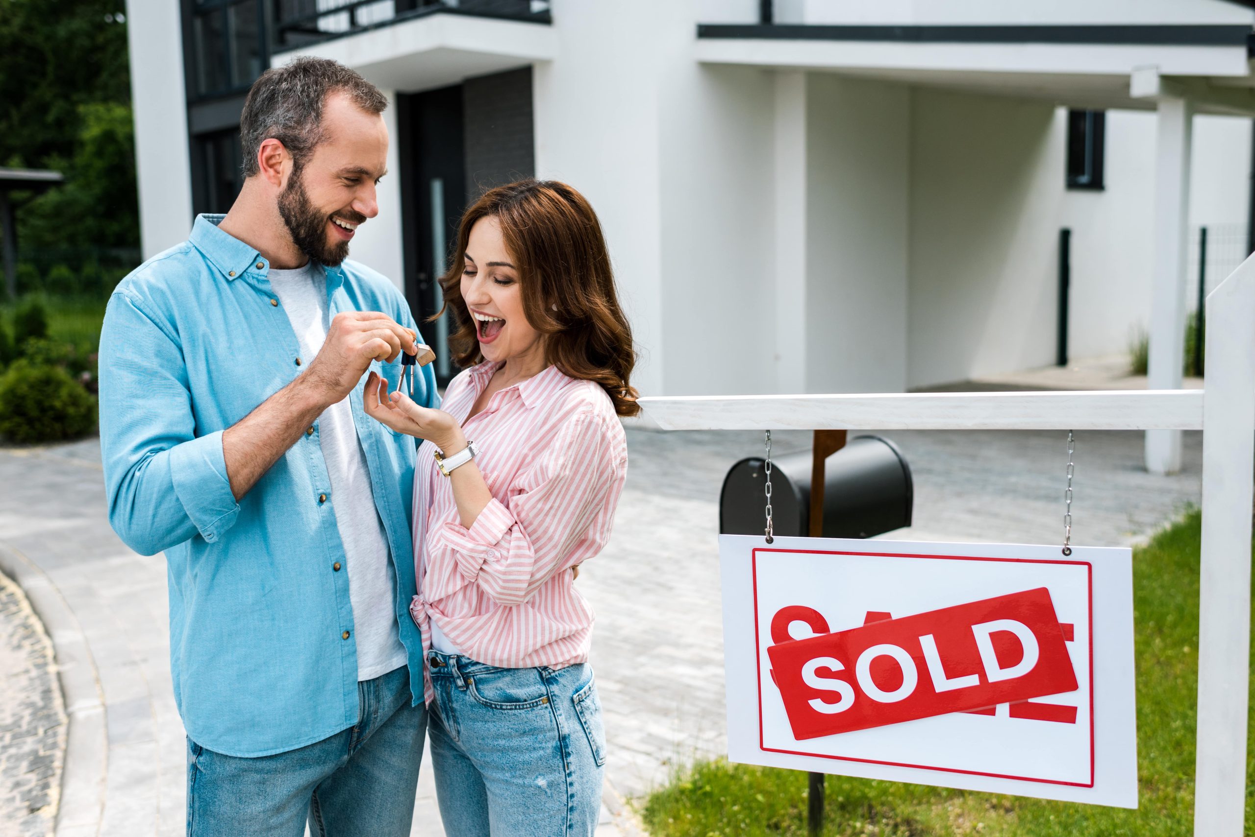 Cheerful couple holding house key in front of sold sign Cheerful couple holding house key in front of sold sign