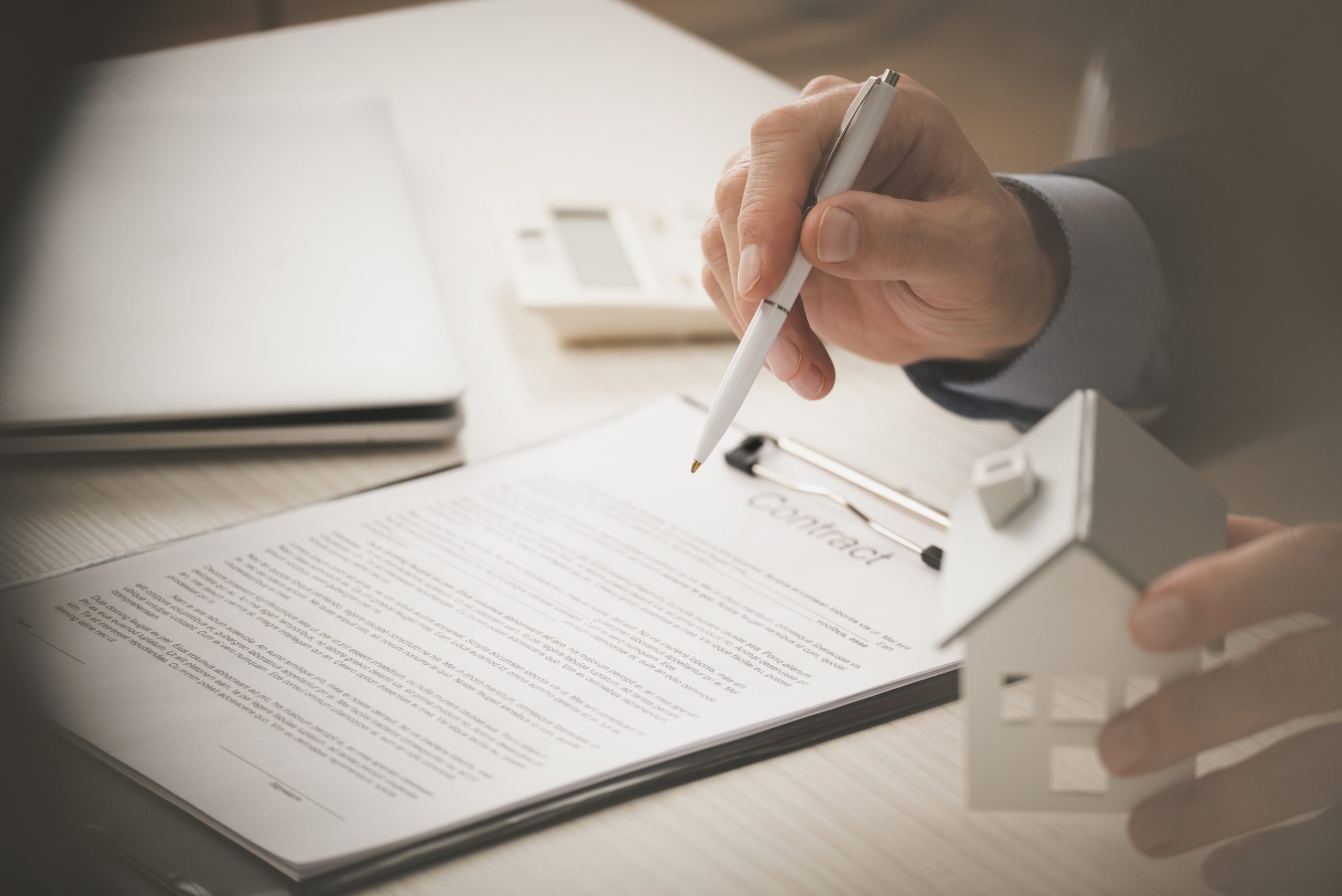 Agent holding pen over a contract with a white house model on desk Agent holding pen over a contract with a white house model on desk